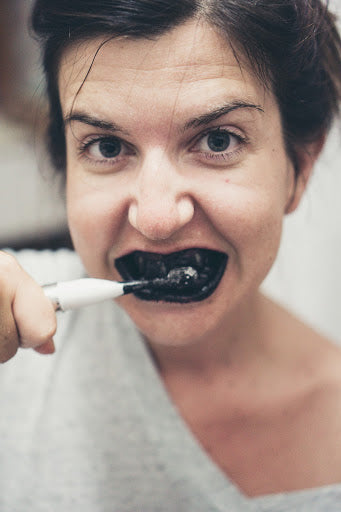 Woman brushing teeth with black, charcoal toothpaste, for AutoBrush blog