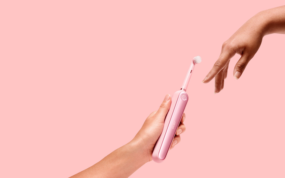 Hand holding a pink automatic toothbrush passing it to another hand, for AutoBrush