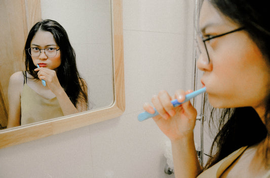 Woman with eyeglasses brushing teeth in front of the mirror, for AutoBrush