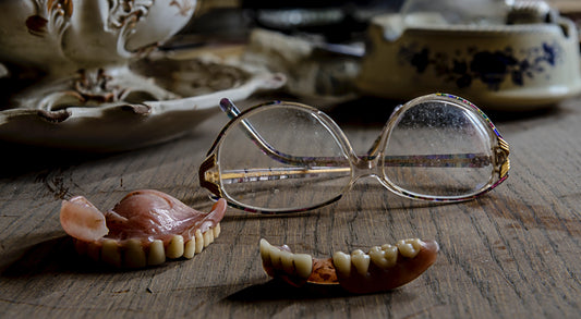 Reading glasses and a pair of dentures on top of a wooden table, for AutoBrush
