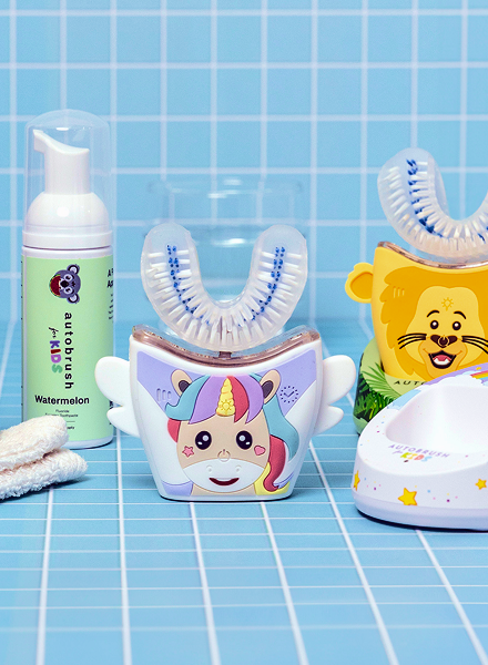 Children's dental care products including a cartoon unicorn-themed toothbrush and a lion-themed brush on a blue tiled background.