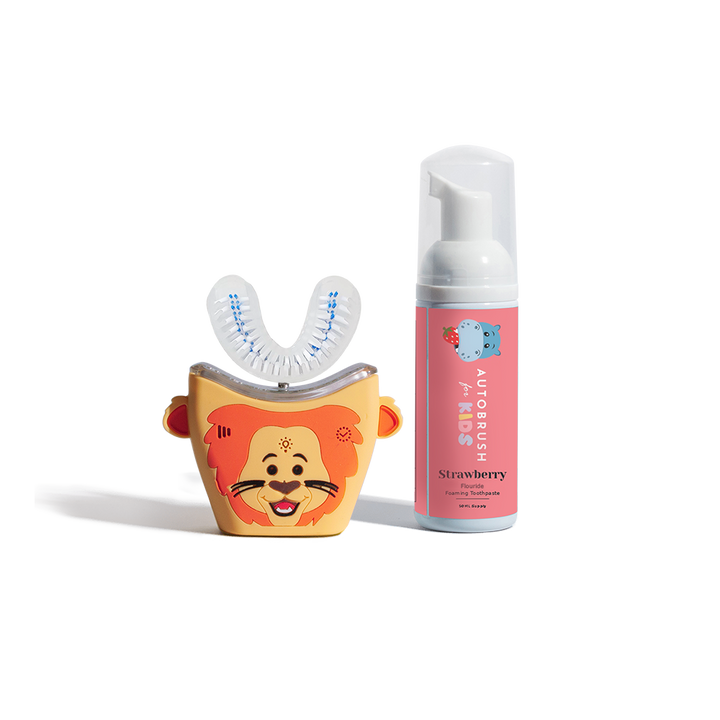 Children’s Autobrush with an orange lion face design, shown next to a pink bottle of strawberry-flavored foaming toothpaste labeled for kids.