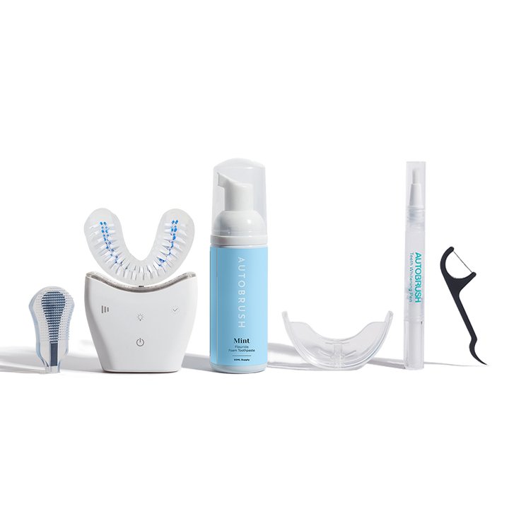 Complete Autobrush set including the white U-shaped brush, mint foaming toothpaste, additional brush heads, a clear mouth tray, whitening pen, and a floss pick.